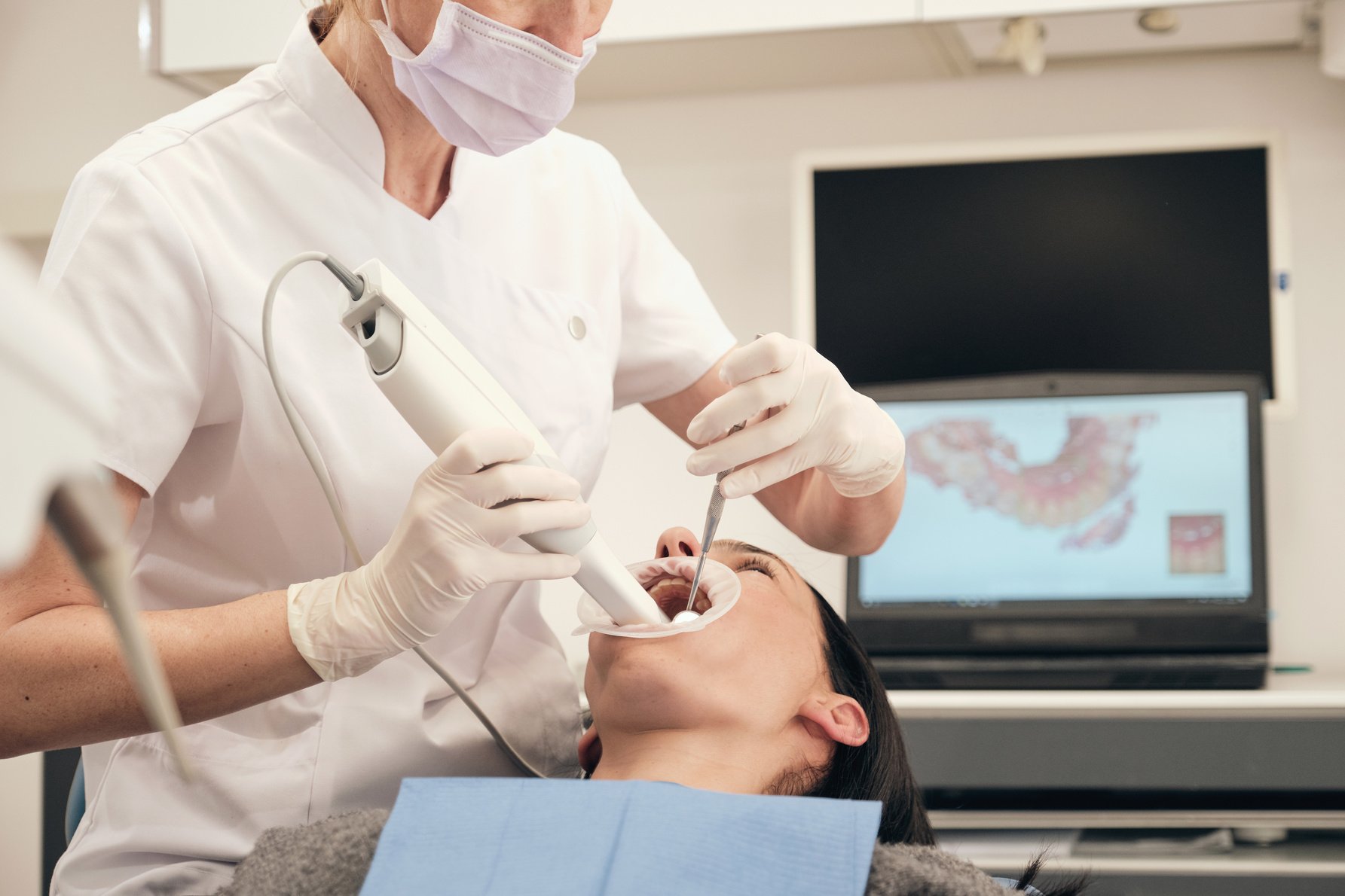 Crop stomatologist scanning teeth of woman in clinic